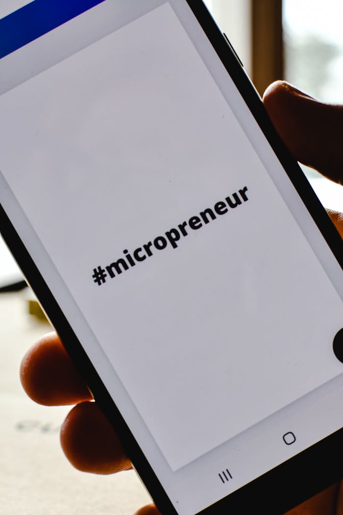 services-03 Close-up of a hand holding a smartphone with the hashtag #micropreneur on screen, symbolizing entrepreneurship.