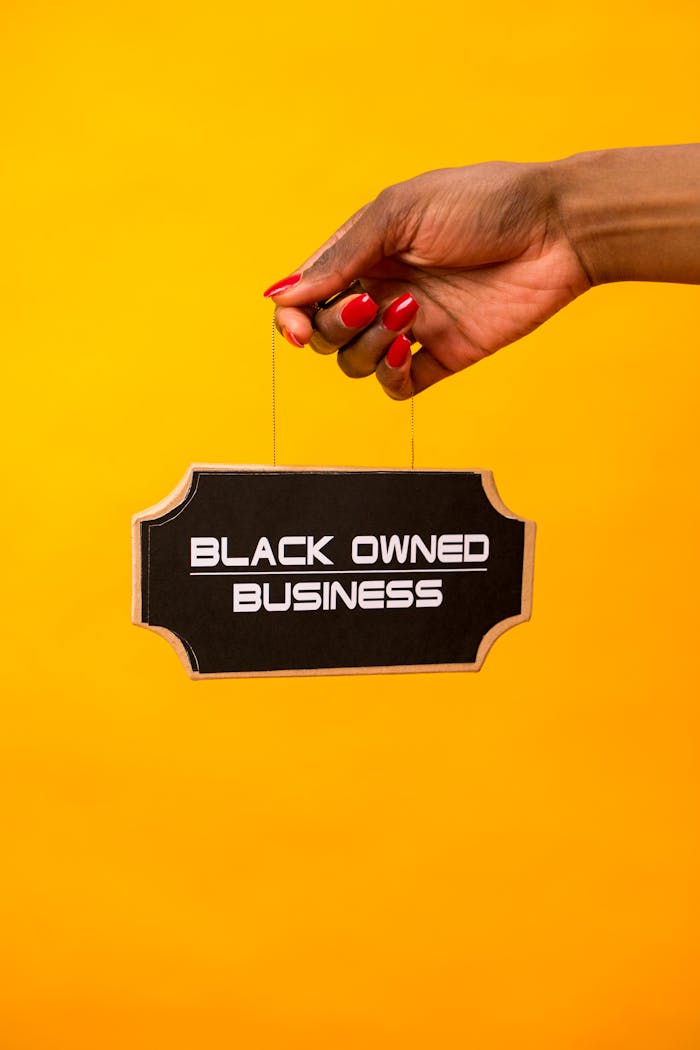 services-01 A hand holds a Black Owned Business sign against a vibrant yellow background.